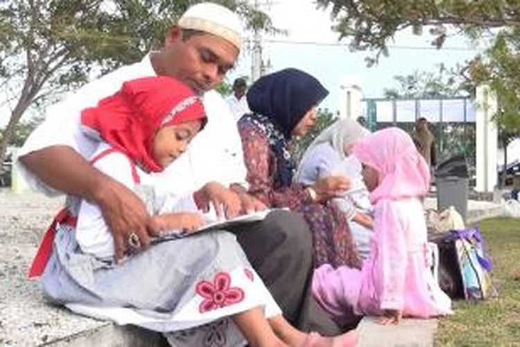 Seorang Ayah sedang menuntun anaknya membaca Surat Yasin di Komplek Makam Massal Korban Tsunami Aceh, Kamis (26/12/2013). Riabuan warga Aceh larut dalam doa dan zikir mengenang sembilan tahun musibah gempa dan tsunami Aceh. *****K12-11