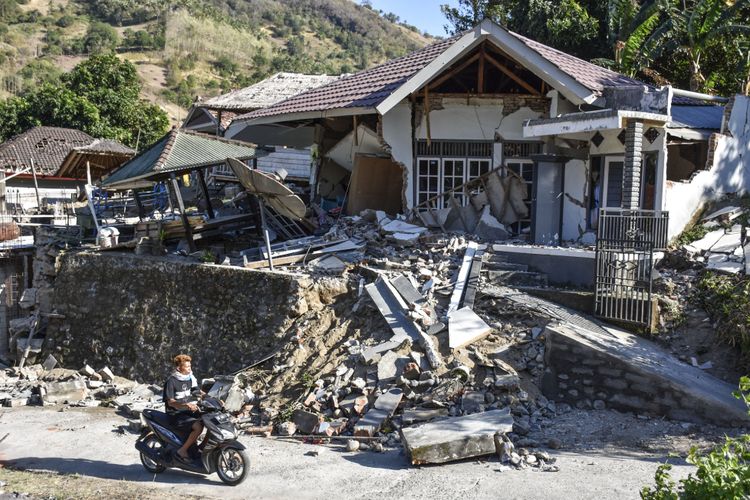 Pengendara sepeda motor melintas dekat rumah yang roboh pascagempa di Desa Bentek, Kecamatan Pemenang,Tanjung, Lombok Utara, NTB, Senin (6/8/2018). Gempa bumi bermagnitudo 7 mengguncang Lombok, Minggu (5/8/2018) malam.