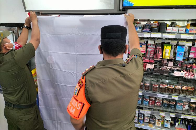 Petugas satpol PP Jakarta Barat menutup display rokok di sebuah minimarket dengan kain putih pada Senin (13/9/2021)