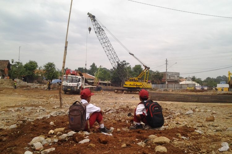 Dua anak SDN 2 Protomulyo Kaliwungu Selatan melihat pengerjaan jalan tol yang berada di belakang sekolahnya.   