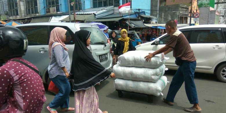Para porter di kawasan Pasar Tanah Abang berjibaku dengan kendaraan untuk mengantarkan barang ke kios ekspedisi, Senin (12/3/2018).