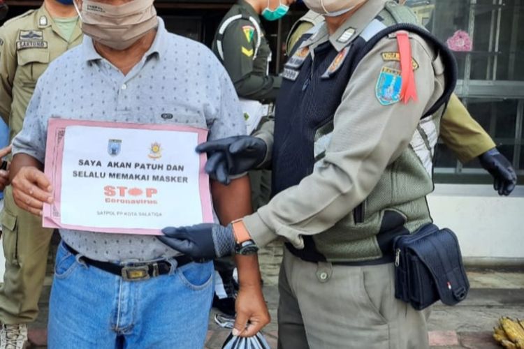 Warga yang tidak memakai masker diharuskan foto menggunakan papan pernyataan. 