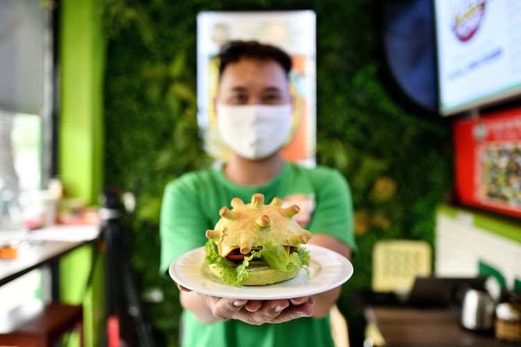 Pemilik Restoran Pizza Home, Hoang Tung, berpose dengan menunjukkan burger bertemakan Virus Corona, di Hanoi, Vietnam, 26 Maret 2020.