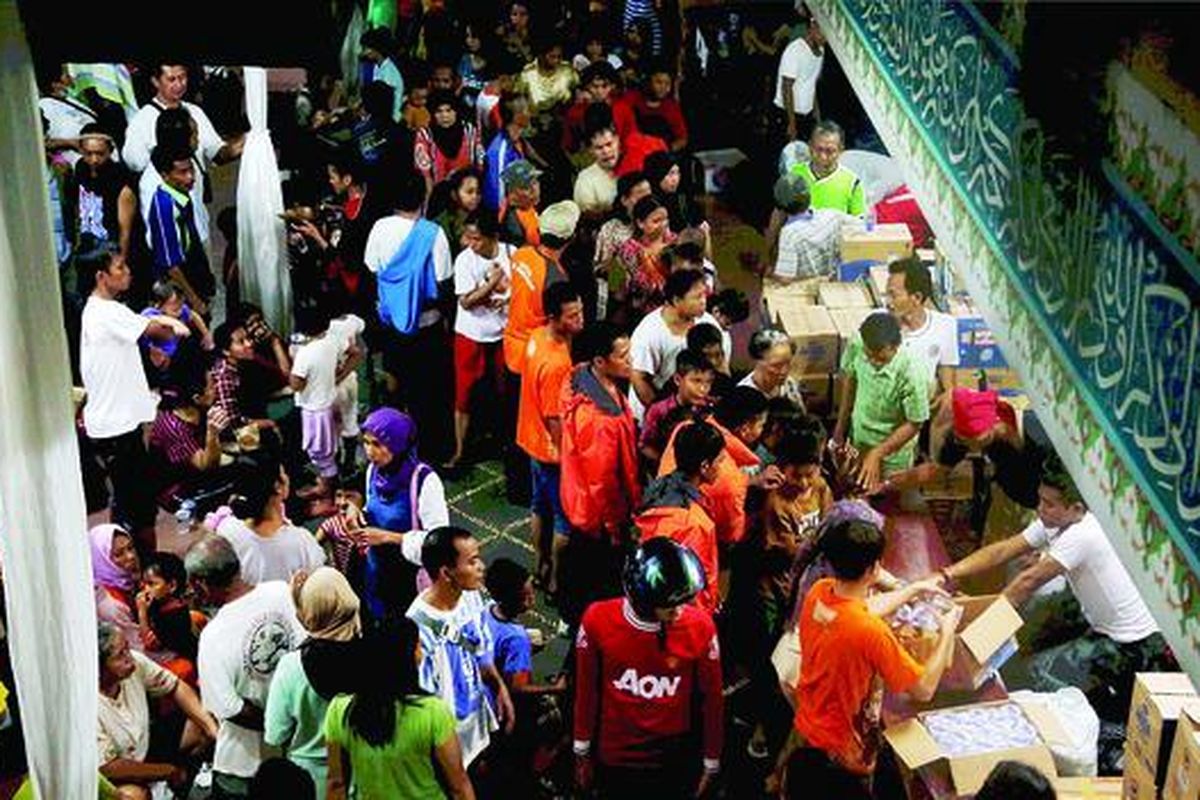Sukarelawan (berbaju oranye) mengatur pembagian nasi bungkus kepada korban banjir yang mengungsi di Masjid Attahiriyah, Kampung Melayu, Jakarta, Jumat (18/1).