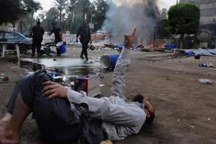 Seorang pria tergeletak di tanah ketika pasukan keamanan Mesir membersihkan kamp yang didirikan oleh para pendukung Presiden Mesir terguling Muhammad Mursi di dekat Universitas Kairo, Giza, Mesir, 14 Agustus 2013.