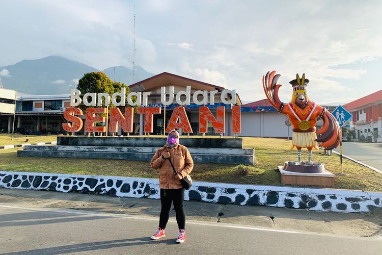 Seorang penumpang pesawat foto berlatar belakang bandara dan maskot PON XX Papua 2021, Drawa.