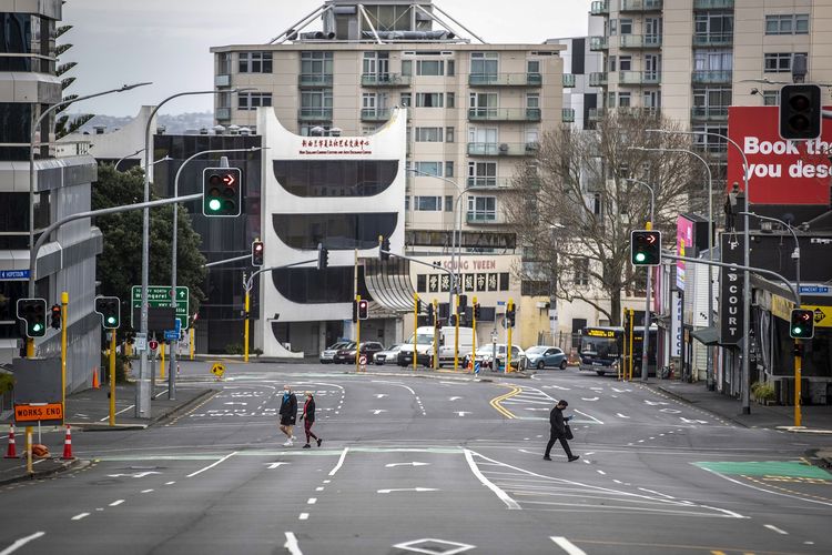 Warga Selandia Baru menyeberangi jalan yang kosong di distrik pusat bisnis Auckland, Jumat (27/8/2021). Selandia Baru lockdown akibat terjadi penyebaran Covid-19 lagi setelah 6 bulan bebas penularan lokal.