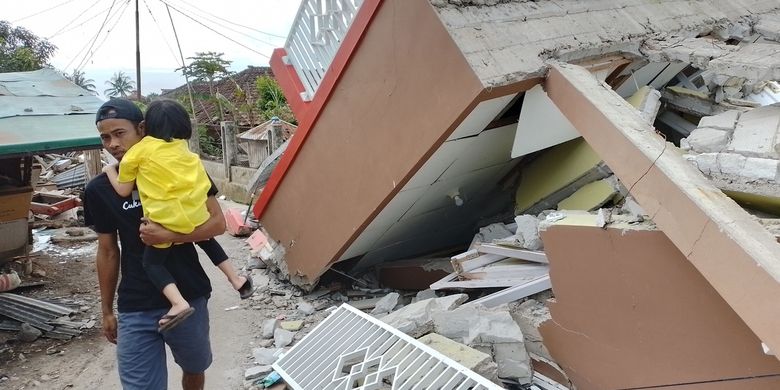 A man carrying a child walking in front of collapsed houses due to a 5.6-magnitude earthquake that struck the city of Cianjur in West Java on Wednesday, November 23, 2022.  