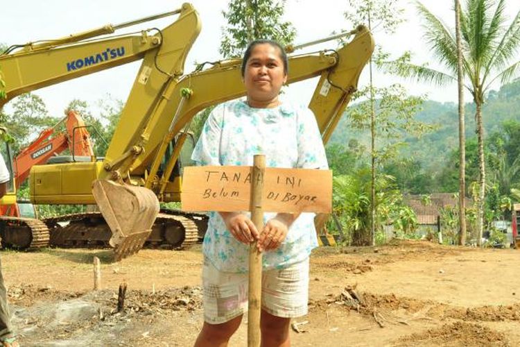 Pemilik tanah dan kandang ayam, Winarni (40) didesa Watuagung, Tuntang, Kabupaten Semarang memegang papan protes dengan latar belakang alat berat.