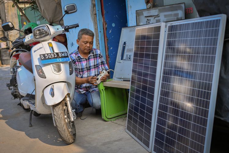 Nur Rohmandi memanfaatkan listrik hasil produksi dari PLTS yang terpasang di bengkel elektronik miliknya untuk mengisi baterai sepeda motor listrik di Kapuk, Jakarta Barat, DKI Jakarta.