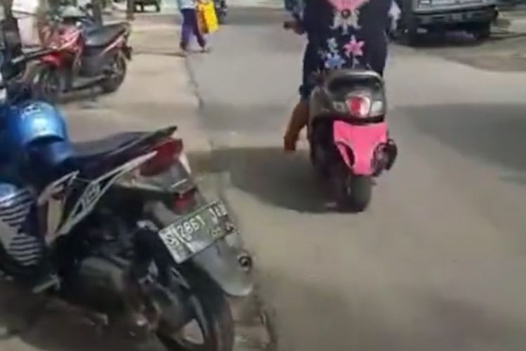 Tangkapan layar video yang memperlihatkan seorang perempuan, sedang mengendarai sepeda motor dengan pelat nomor ditutupi celana dalam di Lamongan. 
