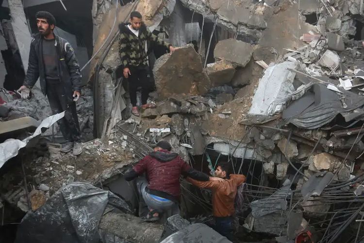 Warga Jalur Gaza di reruntuhan bangunan setelah pemboman oleh Israel, 12 Desember 2023.
