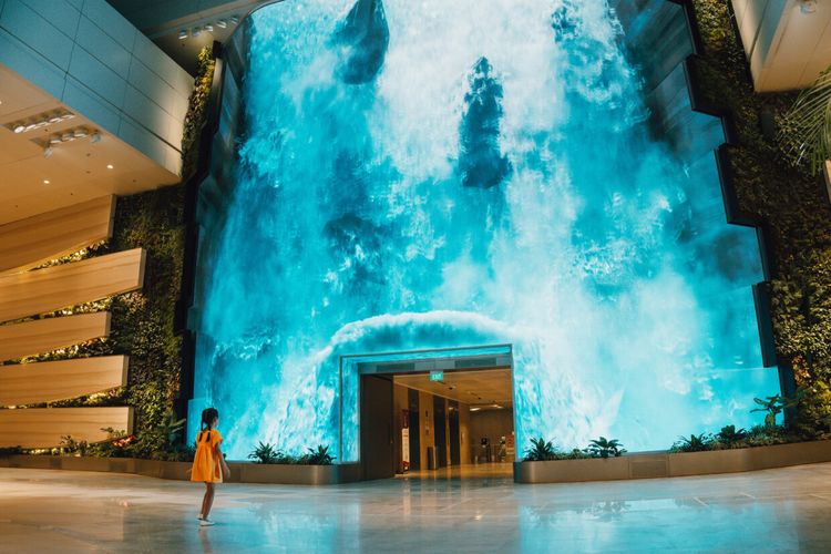 Mengalir ke alam yang menawan dengan turunnya air terjun digital yang megah  di aula keberangkatan T2 Bandara Changi, Singapura. 
