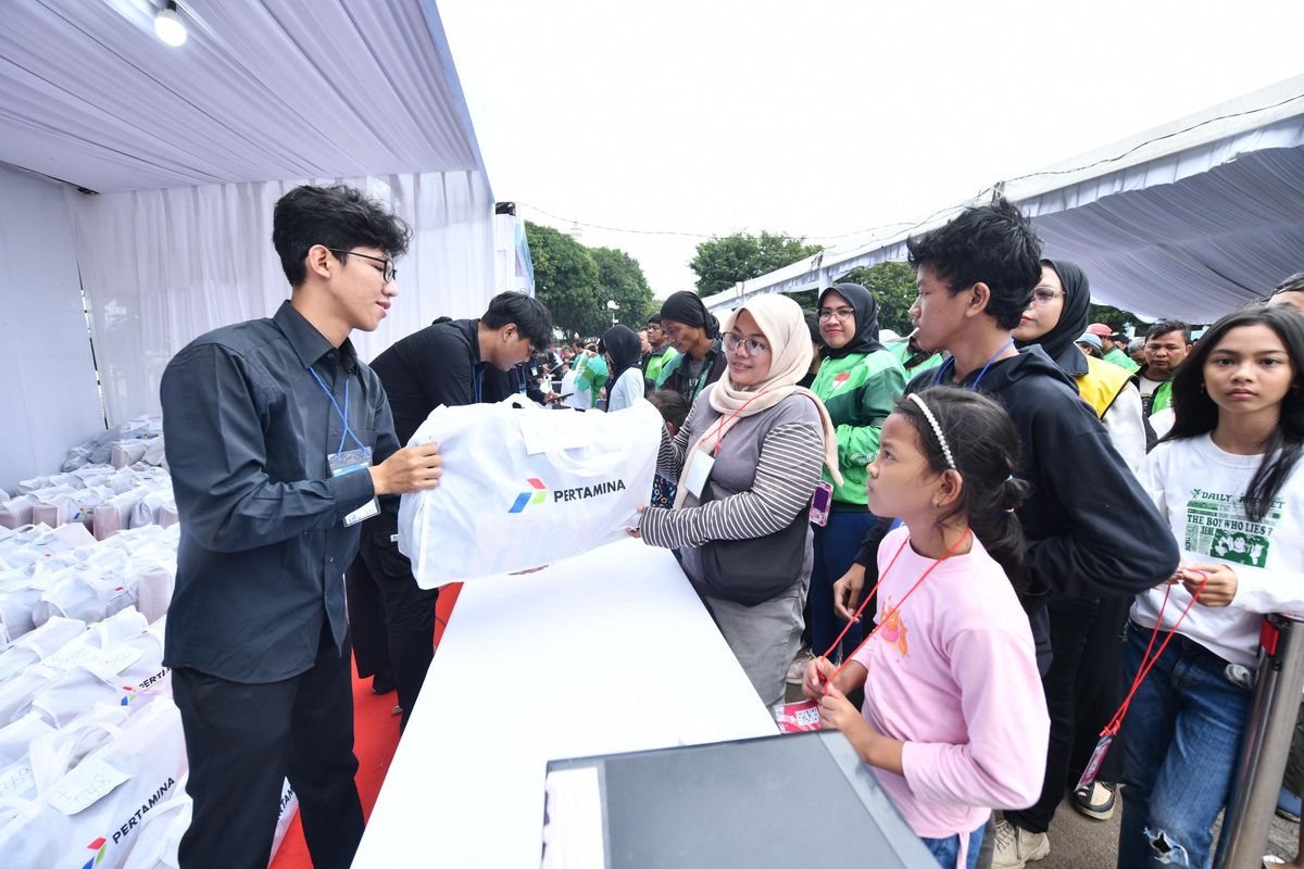 Seorang ibu pengemudi ojek bersama anaknya menerima paket perlengkapan sekolah dari petugas Pertamina dalam program SESAMA di Jakarta, Minggu (13/7/2025)