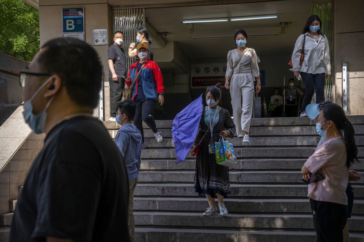 Para komuter yang mengenakan masker berjalan menuruni tangga di stasiun kereta bawah tanah yang baru dibuka kembali di kawasan pusat bisnis di Beijing, Selasa, 31 Mei 2022. 