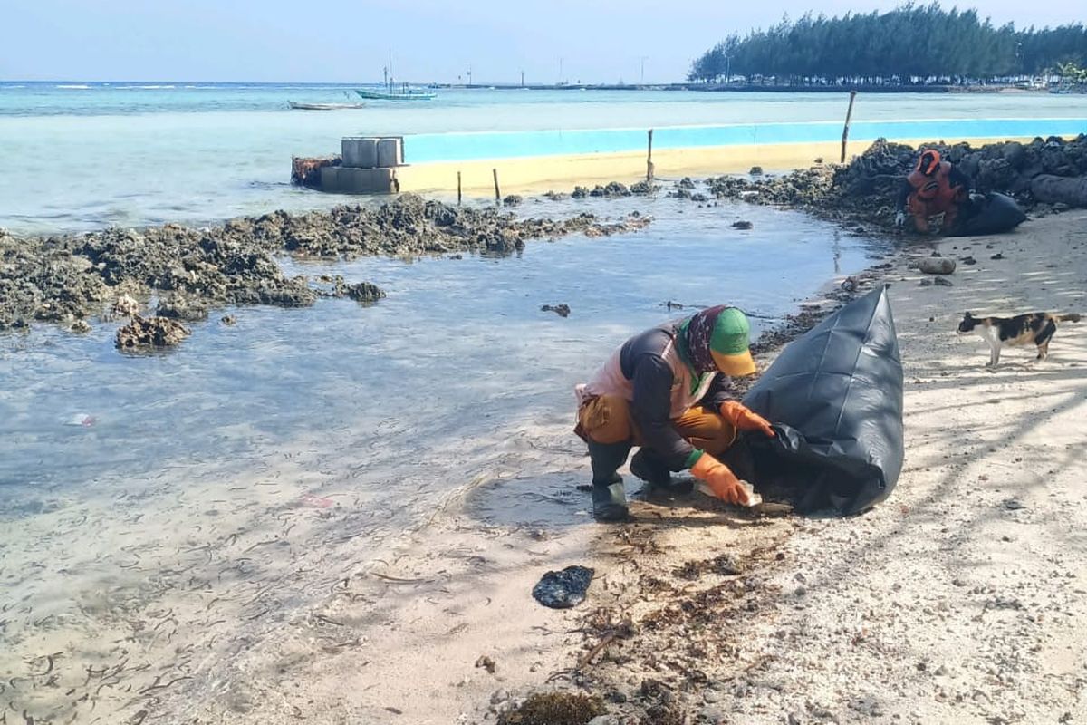 Petugas PPSU Kep Seribu mengumpulkan tumpahan minyak yang sudah berubah menjadi padat di pinggir pantai Pulau Pari, Kep. Seribu, Rabu (12/8/2020)