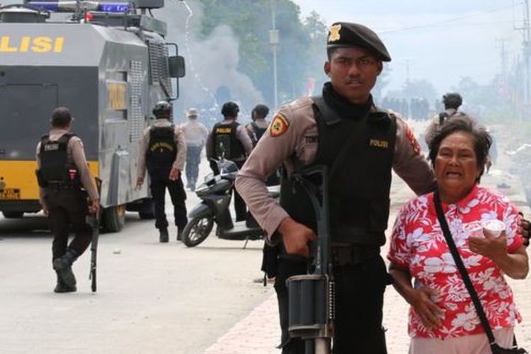 Petugas polisi mengantar seorang ibu menjauh dari pusat kerusuhan di Mimika, Papua Barat. 