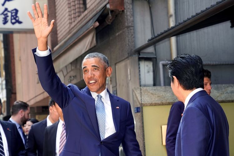 Mantan presiden Amerika Serikat Barack Obama melambai ke media di samping Perdana Menteri Jepang Shinzo Abe, di depan sebuah restoran sushi di distrik perbelanjaan Ginza, Tokyo, Jepang, Minggu (25/3/2018). (AFP/Shizuo Kambayashi)