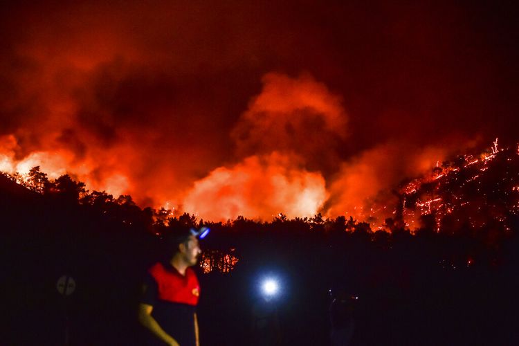 Seorang pria pergi saat kebakaran semakin membesar di daerah Hisaronu, Turki, Senin, 2 Agustus 2021. 