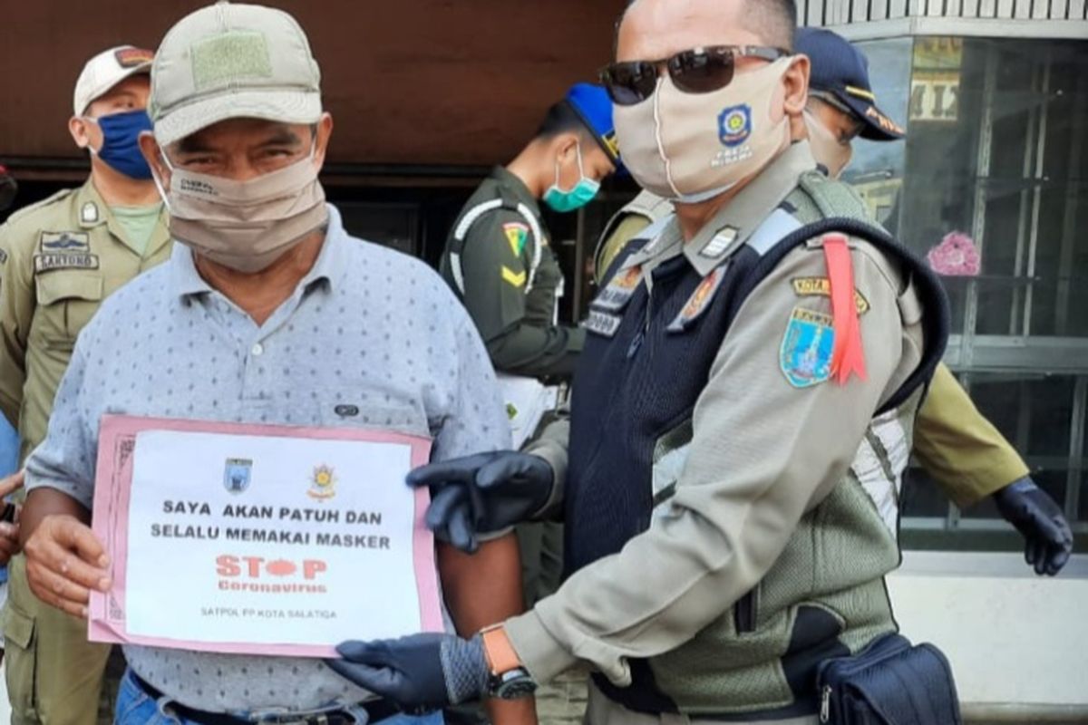 Warga yang tidak memakai masker diharuskan foto menggunakan papan pernyataan. 