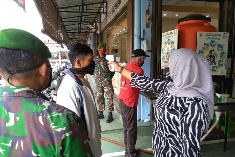 Petugas di pasar Sei Sikambing mengecek suhu tubuh dan masker pengunjung sebelum masuk ke dalam. Pengunjung di mall dan pasar tradisional yang tidak menjalankan protokol kesehatan dilarang masuk.