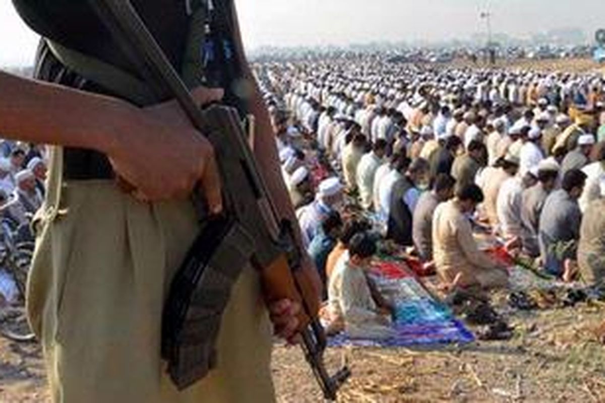 Seorang polisi Pakistan berjaga-jaga ketika para pengungsi Afganistan melaksanakan shalat Idul Adha di Peshawar, Jumat (27/10/2012). Pemerintah Pakistan akan menghentikan sementara layanan telepon seluler terkait laporan intelijen tentang ancaman serangan pada hari pertama masa libur Idul Adha di negara itu.  