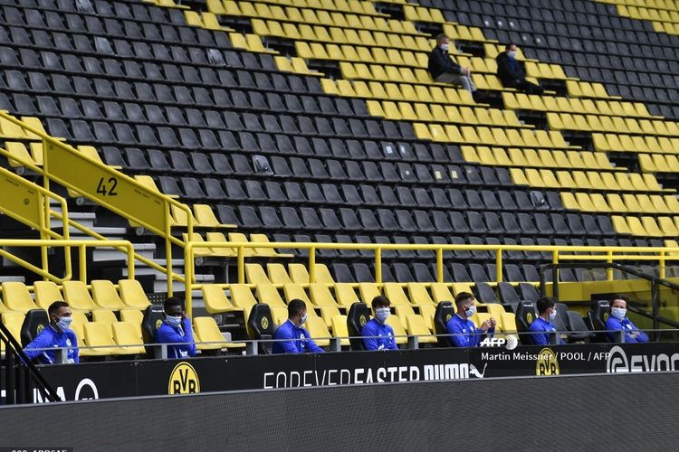 Para pemain Schalke duduk di bangku cadangan yang memerhatikan aspek physical distancing di laga Borussia Dortmund vs Schalke pada 16 Mei 2020.