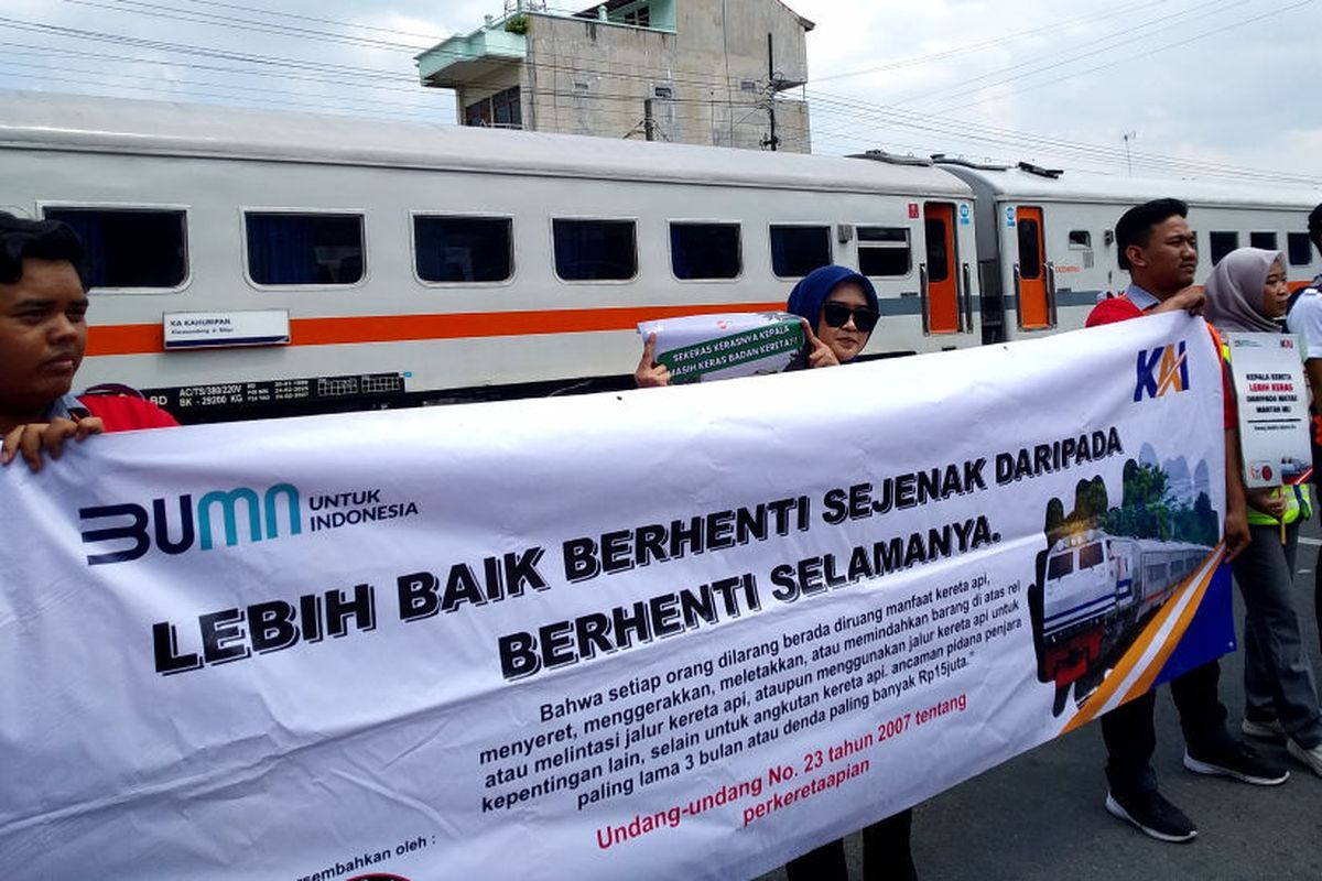 Sejumlah orang membentangkan spanduk berisi himbauan kewaspadaan bagi pengguna jalan di perlintasan sebidang Jalan Anggrek, Kota Blitar, Jawa Timur, oleh PT KAI Daop 7 dan komunitas pecinta kereta api, Rabu (13/8/2025)