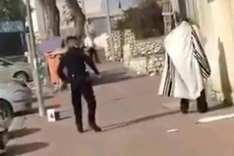 Seorang perwira polisi tertangkap kamera sedang menyemprot lada seorang pria Haredi di Netivot yang sedang berdoa di luar rumahnya pada 7 April 2020.