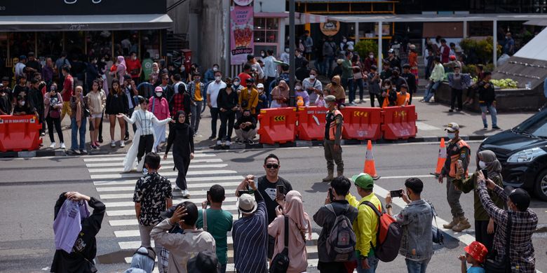 This picture taken on July 24, 2022 shows a crowd looking on as Indonesian youths present self-styled fashion creations at a pedestrian crossing turned catwalk, part of a gathering in recent weeks dubbed Citayam Fashion Week, in Jakarta. The crowd of fashionistas turning one of Jakarta's main commuter hubs into a makeshift catwalk have courted controversy in Indonesia's traffic-clogged capital, but their festival of style has become a site for free expression. (Photo by BAY ISMOYO / AFP) 