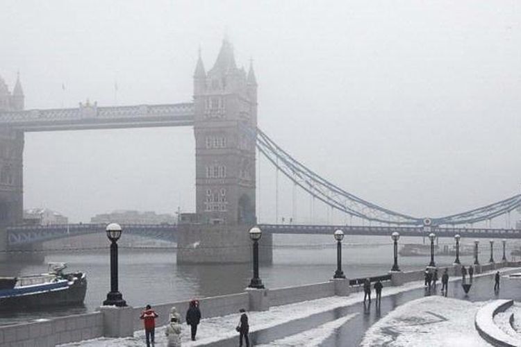 Orang-orang yang baru turun dari kereta berjalan kaki ke tempat kerja di sepanjang sisi Sungai Thames yang bersalju