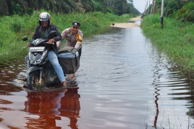 Seorang anggota polisi mendorong sepeda motor warga yang mogok akibat menerobos banjir di Jalan Perkebunan, Desa Merbau, Kecamatan Bunut, Kabupaten Pelalawan, Riau, Rabu (31/1/2024).