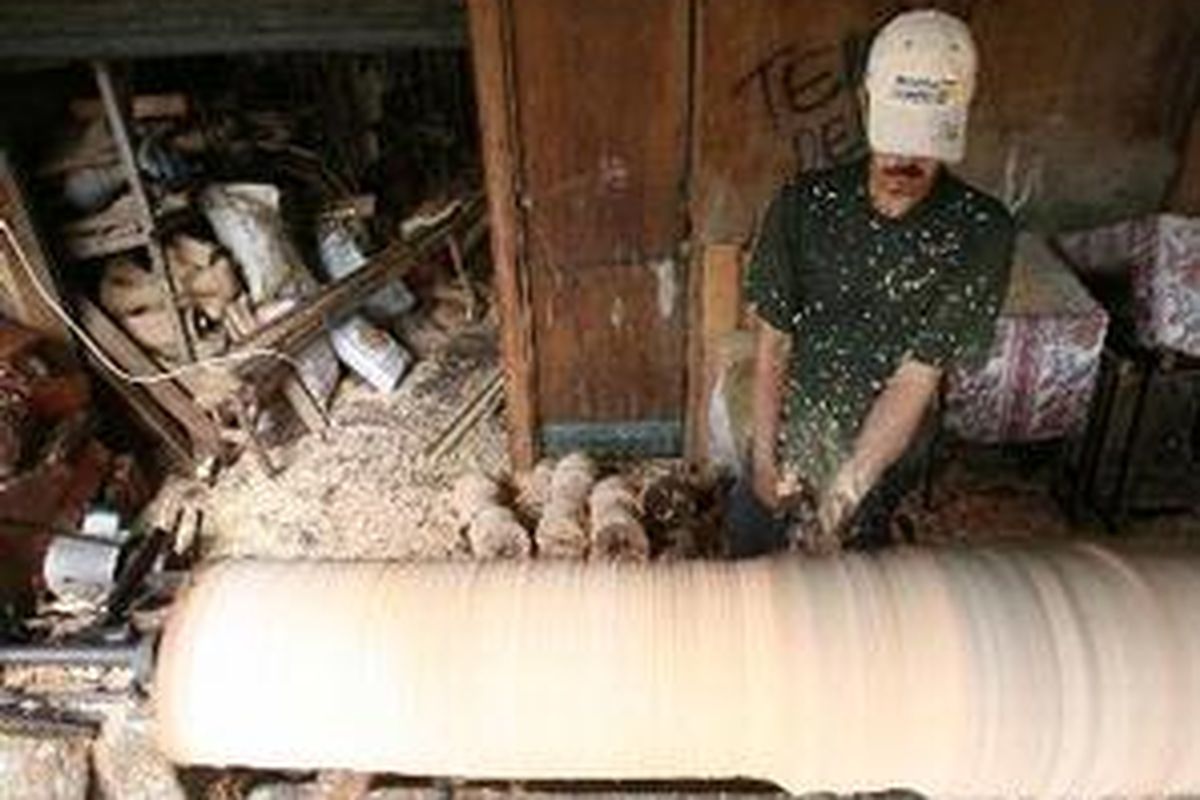 Seorang pekerja sedang membersihkan kulit batang pohon kelapa.