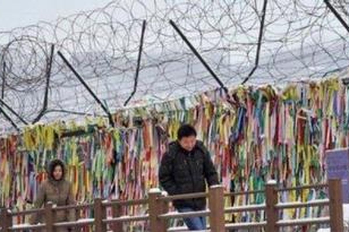 Sejumlah pengunjung berjalan melintasi pagar kawat yang dihiasi pita di Zona Demiliterisasi yang memisahkan kedua Korea. Pagar kawat berhias pita ini kerap disebut "Reunification Ribbon".