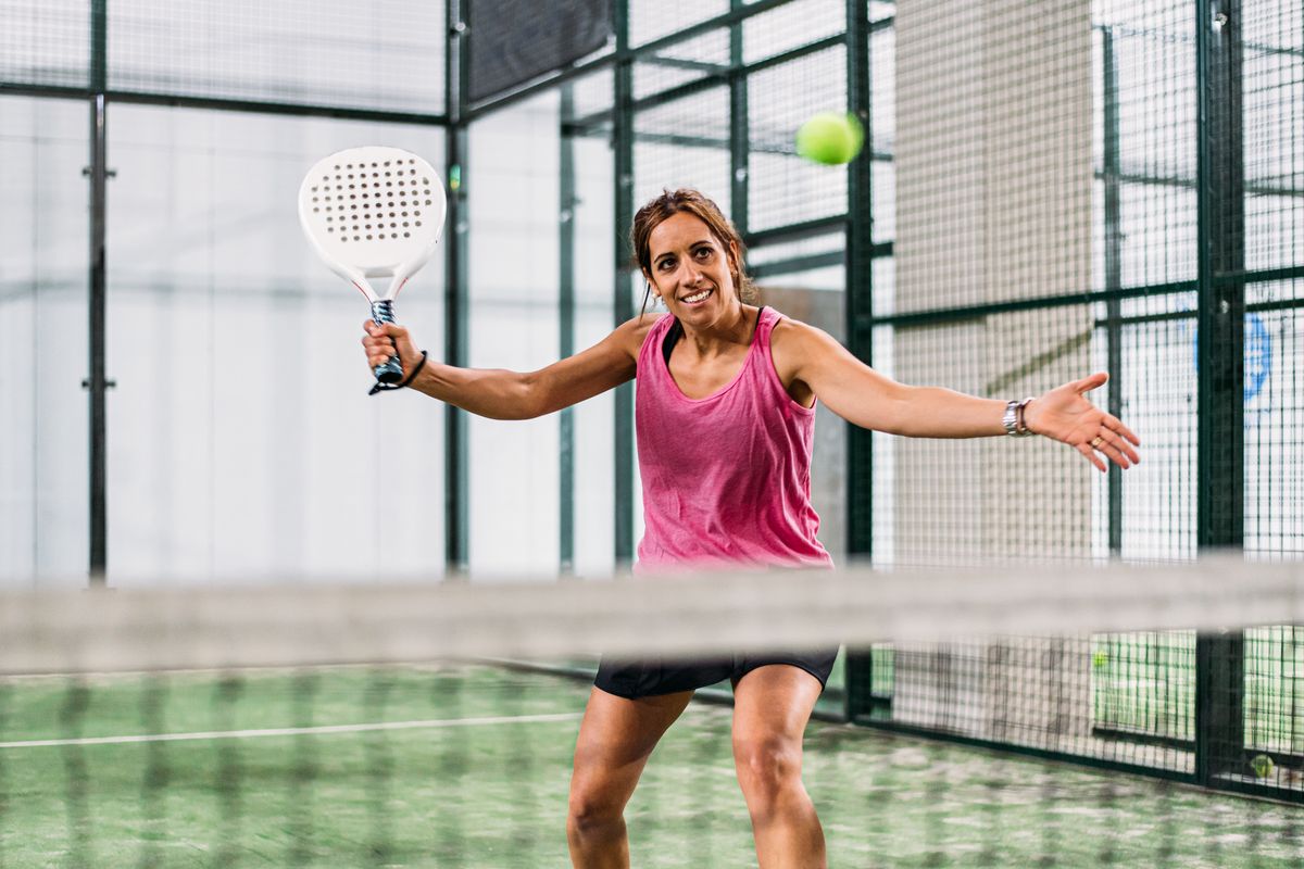Seorang perempuan bermain padel di lapangan padel rumput hijau dalam ruangan.