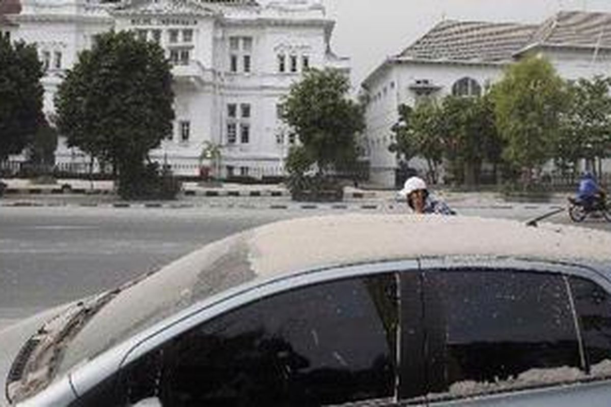 Warga melintas disamping kendaraan yang diselimuti abu vulkanik akibat letusan Gunung Merapi di Jalan Pangeran Senopati, Yogyakarta, Sabtu (30/10/2010). 