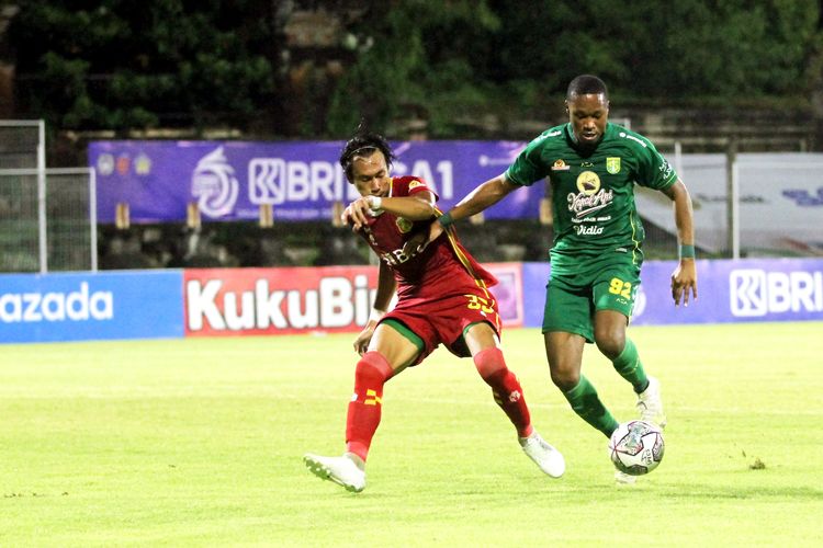 Pemain asing Persebaya Surabaya Arsenio Valpoor dijaga pemain Bhayangkara FC Hansamu Yama pada pertandingan pekan 20 Liga 1 2021-2022 yang berakhir dengan skor 2-1 di Stadion I Gusti Ngurah Rai Denpasar, Selasa (18/1/2021) malam.