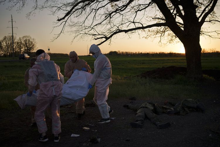 Pekerja darurat Ukraina membawa mayat seorang tentara Rusia di desa Vilkhivka, baru-baru ini direbut kembali oleh pasukan Ukraina di dekat Kharkiv, Ukraina, Senin, 9 Mei 2022.