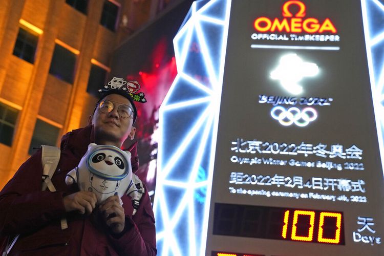 A supporter of the 2022 Beijing Winter Olympics poses for photos with a countdown clock as it crosses into the 100 days countdown to the opening of the Winter Olympics in Beijing, China, Tuesday, Oct. 26, 2021. (AP Photo/Ng Han Guan) ///