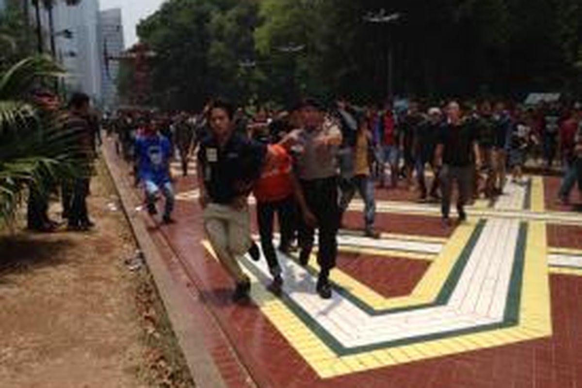 Polisi berlarian menembus rombongan suporter sambil mengamankan remaja yang melempari suporter dengan petasan dan batu di dekat akses masuk Stadion Utama Gelora Bung Karno (SUGBK), Minggu (18/10/2015). 



