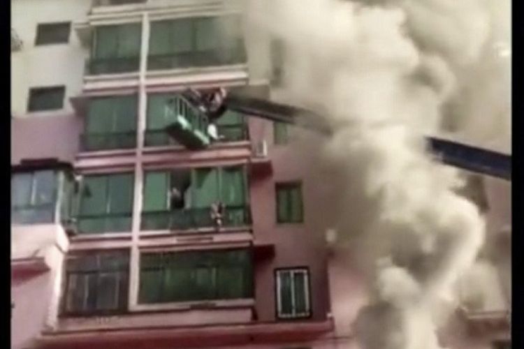 Foto yang menunjukkan lengan dari mesin crane menjangkau orang-orang yang terjebak di bangunan yang terbakar di China.