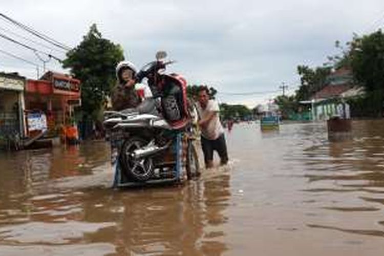 Salah satu tukang becak mengangkut sepeda motor yang terjebak banjir di ruas Jalur Pantura, Desa Tambakrejo, Kecamatan Kraton, Kabupaten Pasuruan, Jawa Timur, Kamis (30/6/2016)