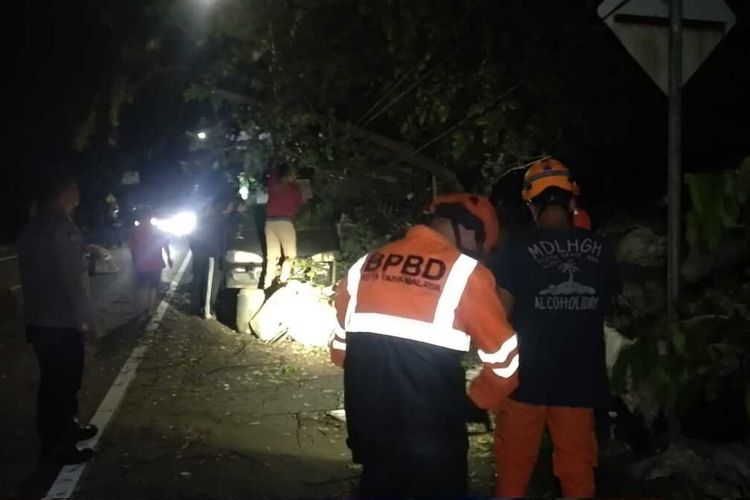 Petugas Kepolisian dan BPBD Kota Tasikmalaya membersihkan reruntuhan pohon tumbang akibat angin kencang di Jalan Ibrahim Adji, Indihiang, Kota Tasikmalaya, Jawa Barat, Minggu (26/2/2023).