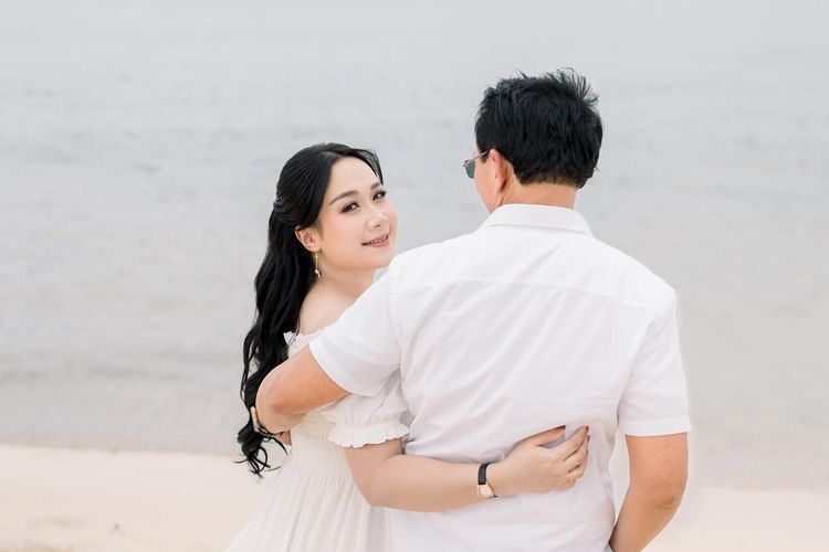 Puput Nastiti Devi tampil anggun dengan long dress putih, makeup natural, dan rambut wavy saat foto kehamilan anak ketiga bersama keluarga.