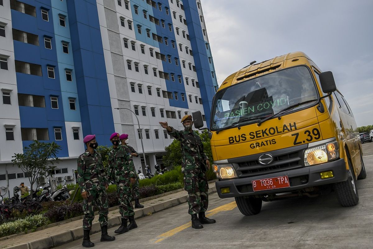 Sejumlah prajurit TNI mengarahkan bus sekolah yang membawa pasien COVID-19 dengan kategori Orang Tanpa Gejala (OTG) di Rumah Susun Nagrak, Cilincing, Jakarta Utara, Senin (21/6/2021). Data Satuan Tugas Penanganan COVID-19 per hari Senin (21/6) menyebutkan kasus positif COVID-19 bertambah 14.536 orang sehingga total menjadi 2.004.445 orang, sementara kasus pasien sembuh bertambah 9.233 orang menjadi 1.801.761 orang, dan kasus meninggal akibat COVID-19 bertambah 294 jiwa sehingga totalnya menjadi 54.956 jiwa. ANTARA FOTO/M Risyal Hidayat/wsj.