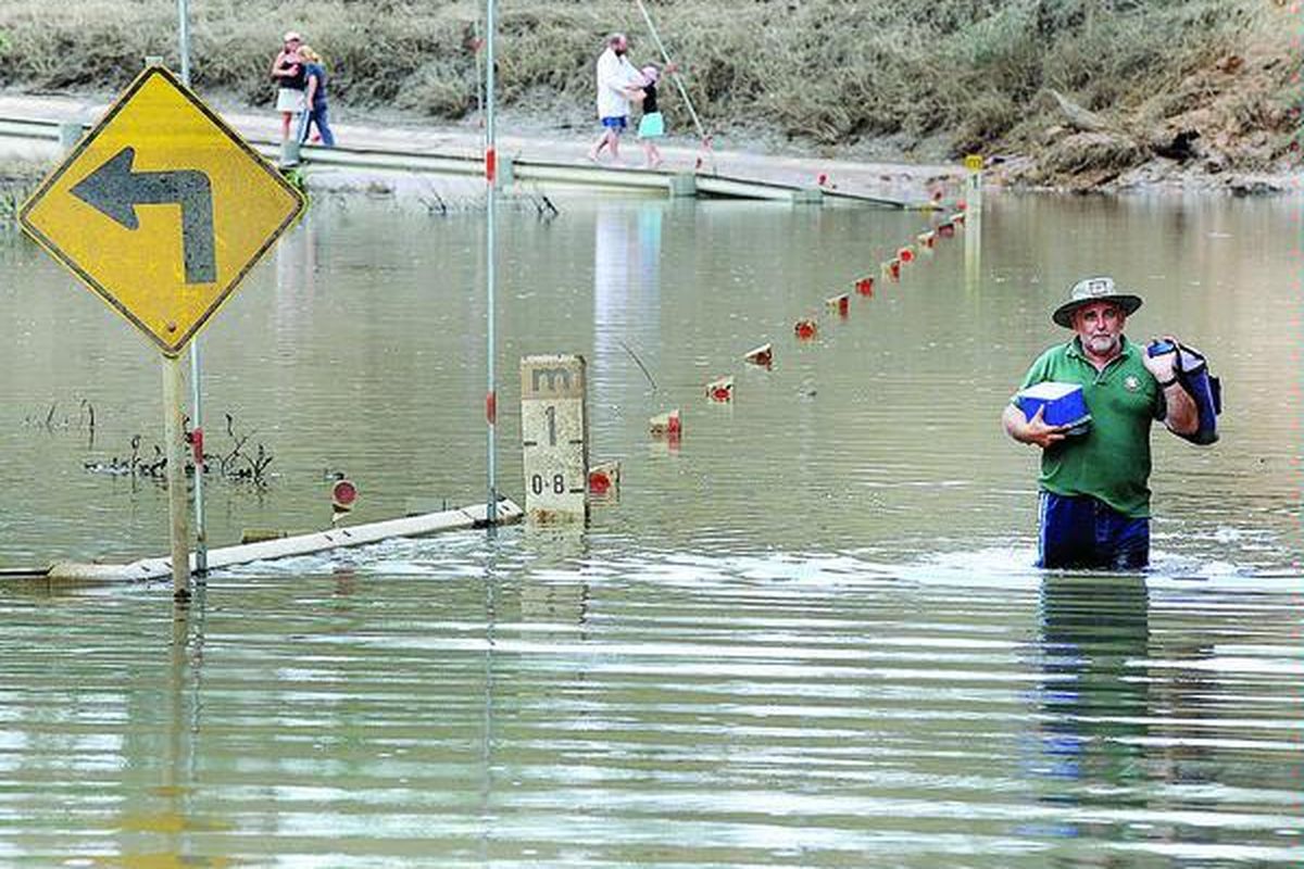 Warga Queensland, Al Ball (kanan), menyeberangi jembatan Sungai Perry yang terendam banjir di kota Gin gin, Minggu (2/1). Sekitar 200.000 warga Negara Bagian Queensland didera banjir bandang dan harus meninggalkan kota tempat tinggal mereka lantaran hampir seluruhnya terendam banjir.