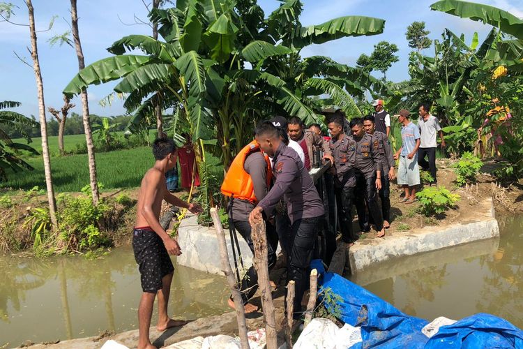 Petugas kepolisian dan warga saat mengevakuasi jenazah korban yang ditemukan, pasca hanyut dan tenggelam di sungai Kali Janggol di Desa Gunungrejo, Kecamatan Kedungpring, Lamongan.