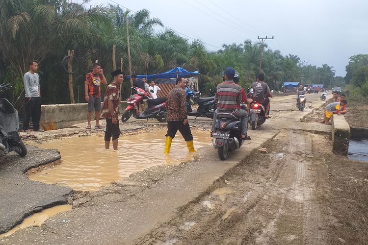 Sejumlah warga melintasi jalan yang rusak akibat banjir di Desa Buluh Cina, Kecamatan Siak Hulu, Kabupaten Kampar, Riau, Senin (6/1/2020).