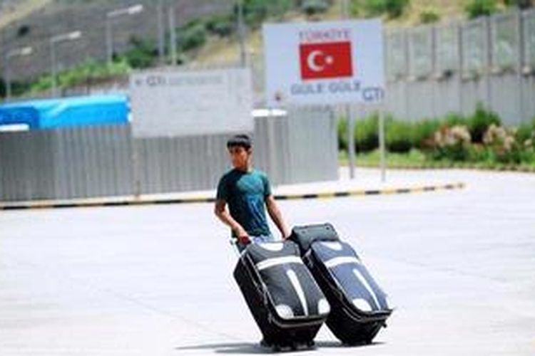 Seorang pengungsi Suriah berjalan sambil membawa koper di depan sebuah spandung bertuliskan "Selamat Jalan" di pintu perbatasan Cilvegozu, Turki. 