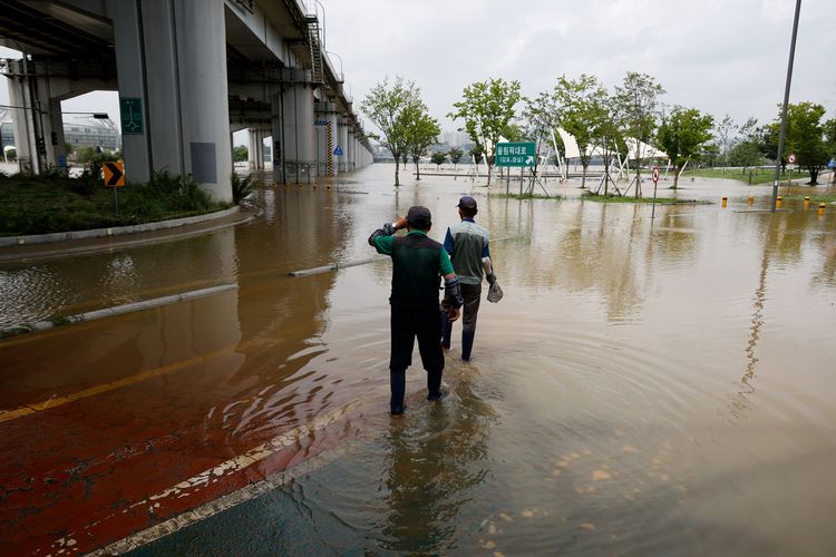 Pekerja berjalan menerjang genangan air di jalan akibat luapan Sungai Han di Seoul, Korea Selatan, pada Selasa (4/8/2020).